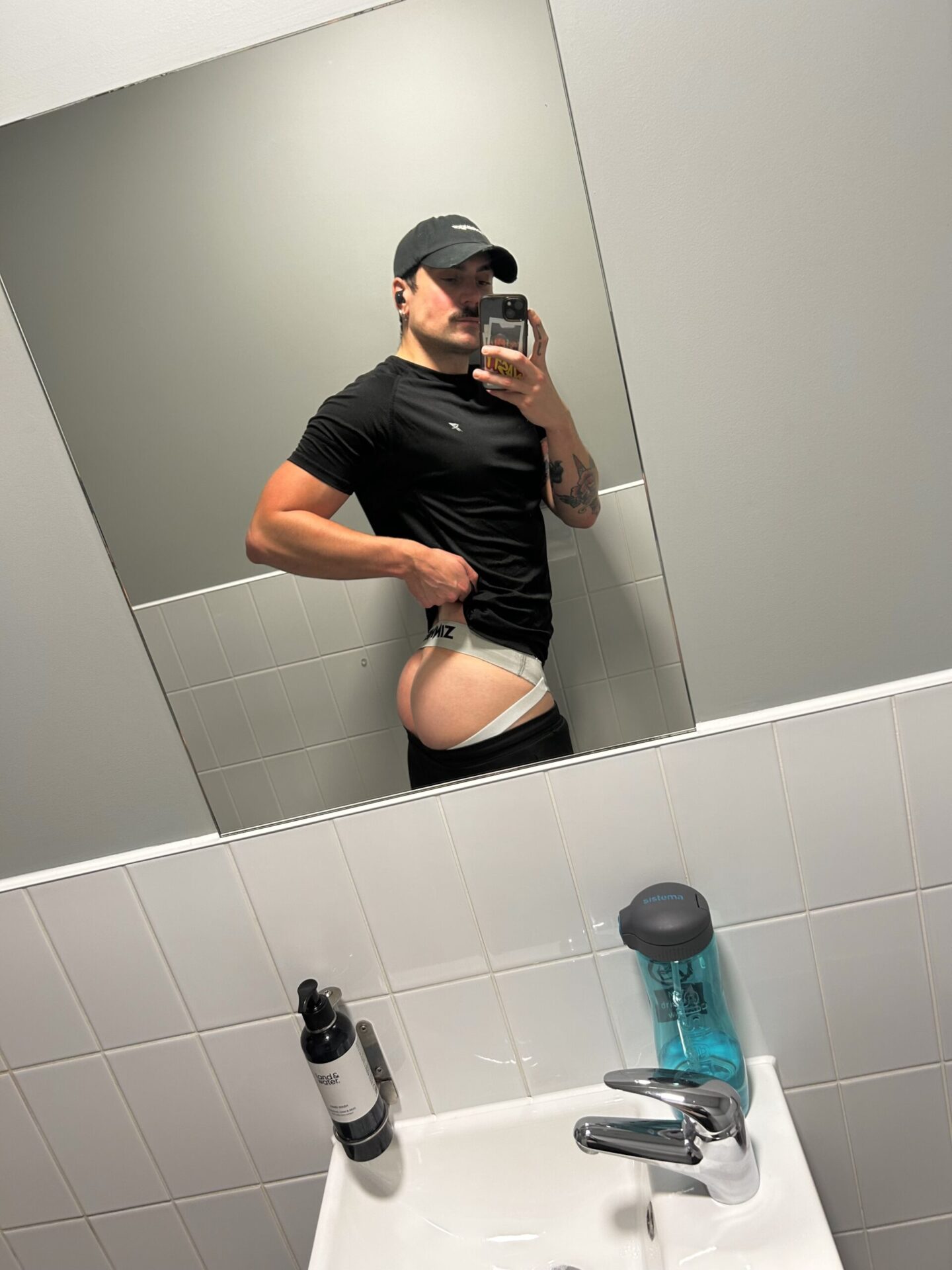 A man smiles as he takes a selfie in the bathroom mirror, capturing a fun moment in his daily routine.